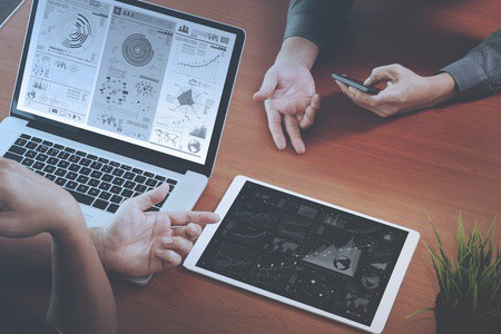 top view of two colleagues discussing data with new modern computer laptop and pro digital tablet with digital business strategy layer effect on wooden desk 