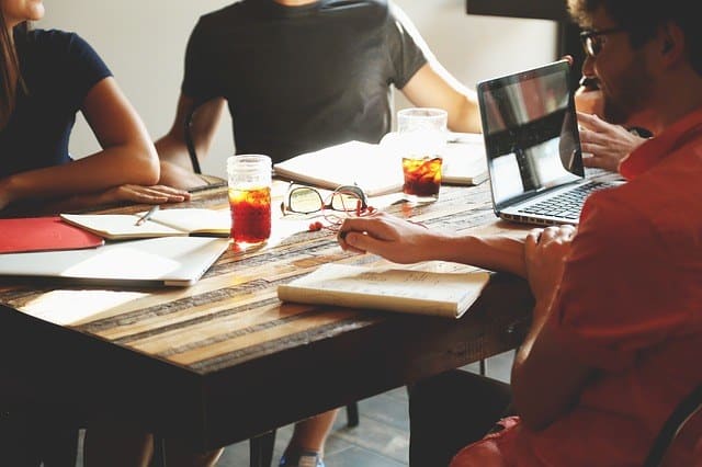 cafe table top showing people working together with cokes, pens, papers and laptops. Trying to suggest you should pick a SEO partner. 