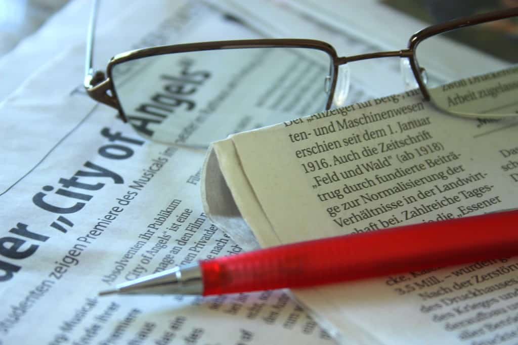 pen an glasses sitting on top of a newspaper article